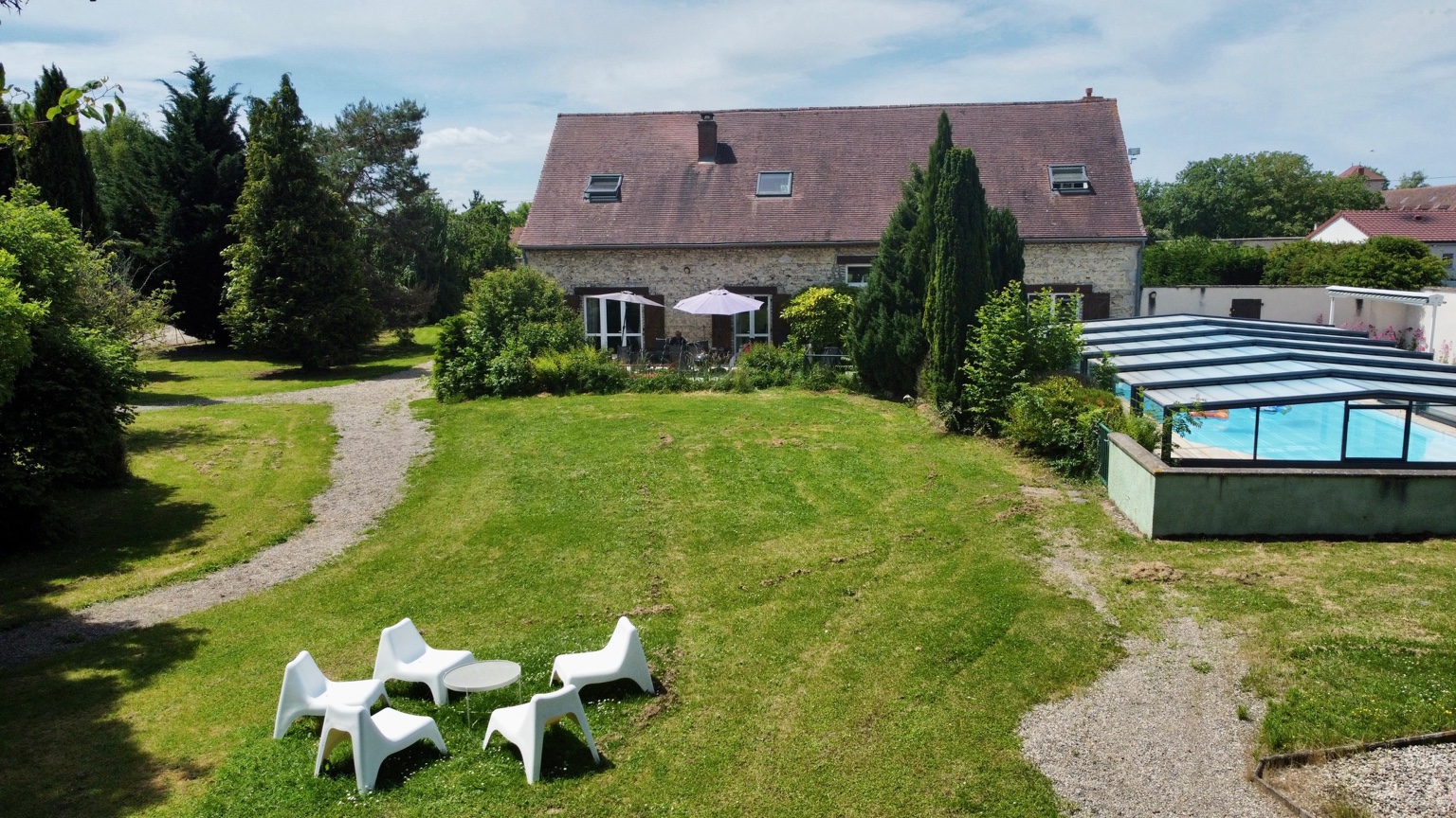 Vue aérienne de l’arrière de la maison, du jardin, des chaises blanches sur la pelouse et de l’abri de piscine
