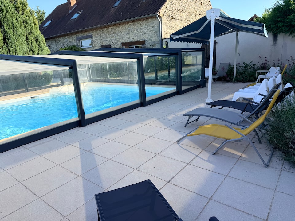 Piscine sous son abri vitré avec espace de détente sur la terrasse